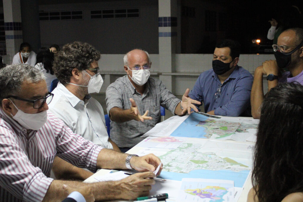 Pessoas sentadas discutindo, com mapas sobre a mesa