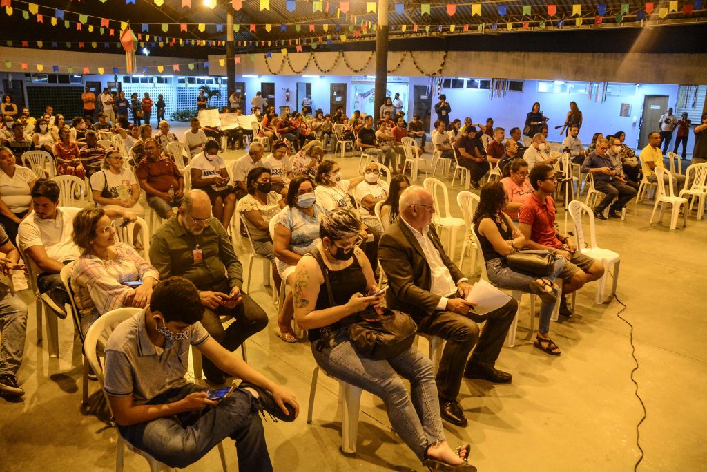 Pessoas sentadas em cadeiras em um barracão.